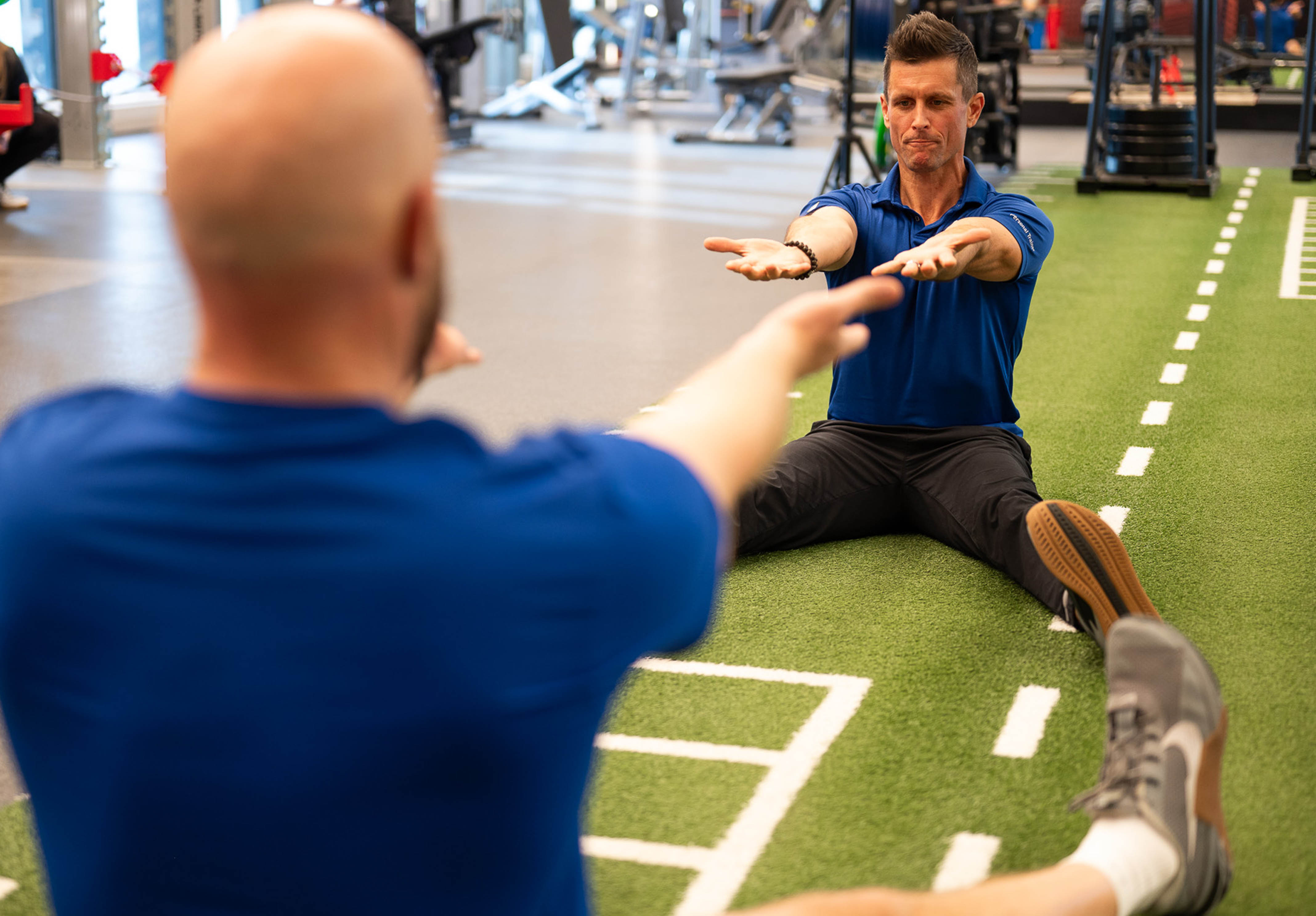 Two male trainers doing mobility work and stretching on the turf in the Strength Lab at the Toronto Athletic Club