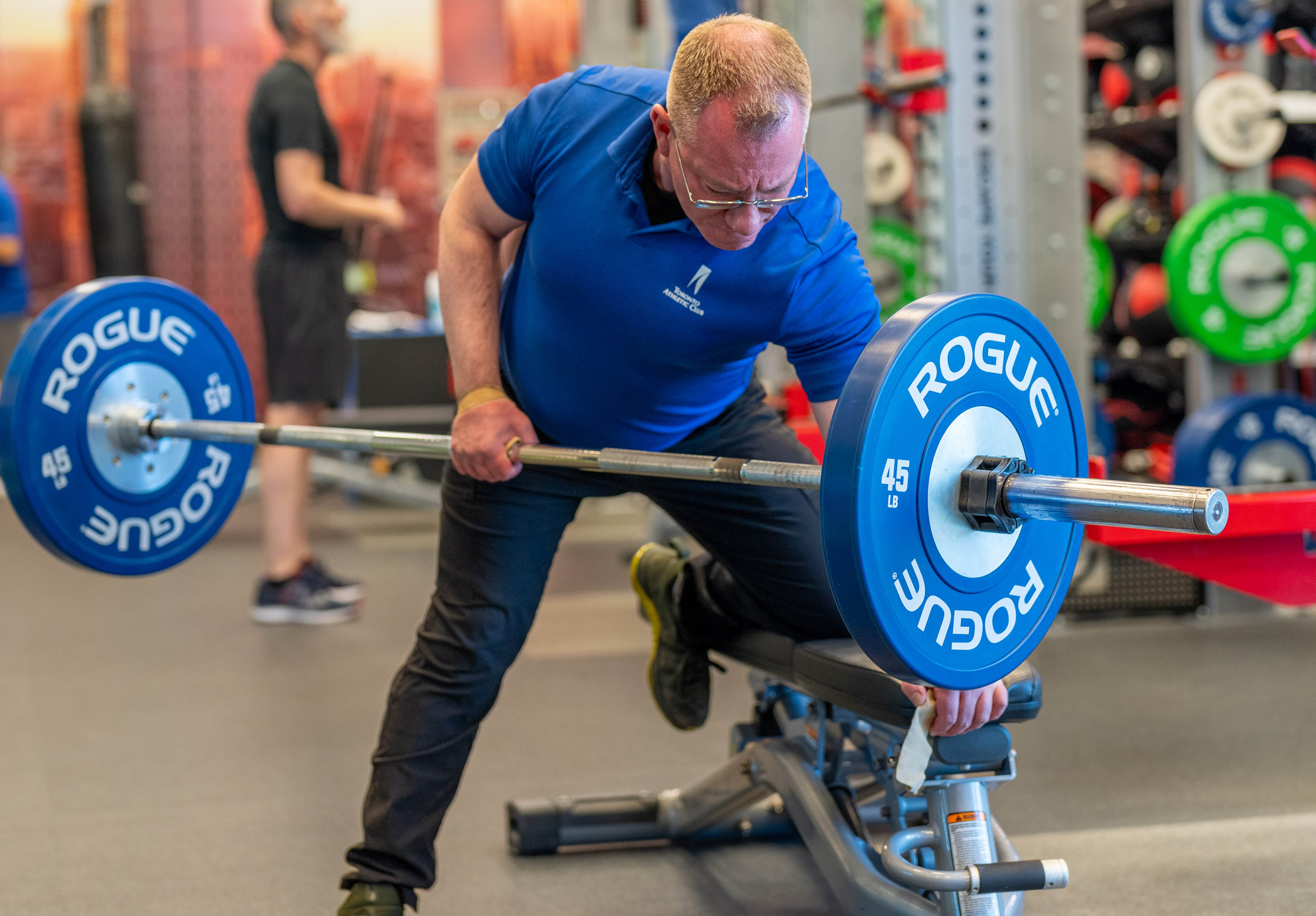 Male trainer at the Toronto Athletic Club doing a one arm weighted lift with a barbell in the Strength Gym